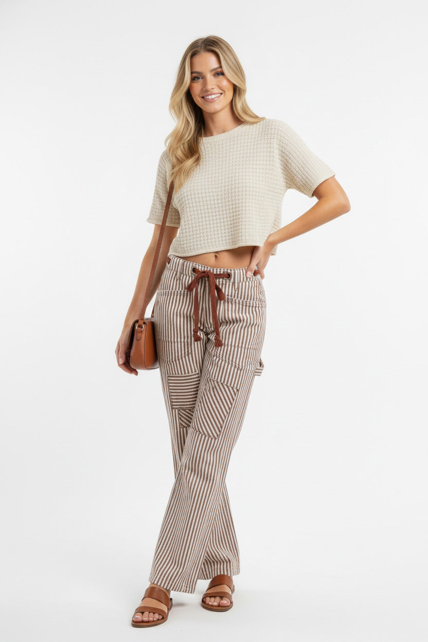 Woman wearing a white top and striped pants with a brown bag on a white background