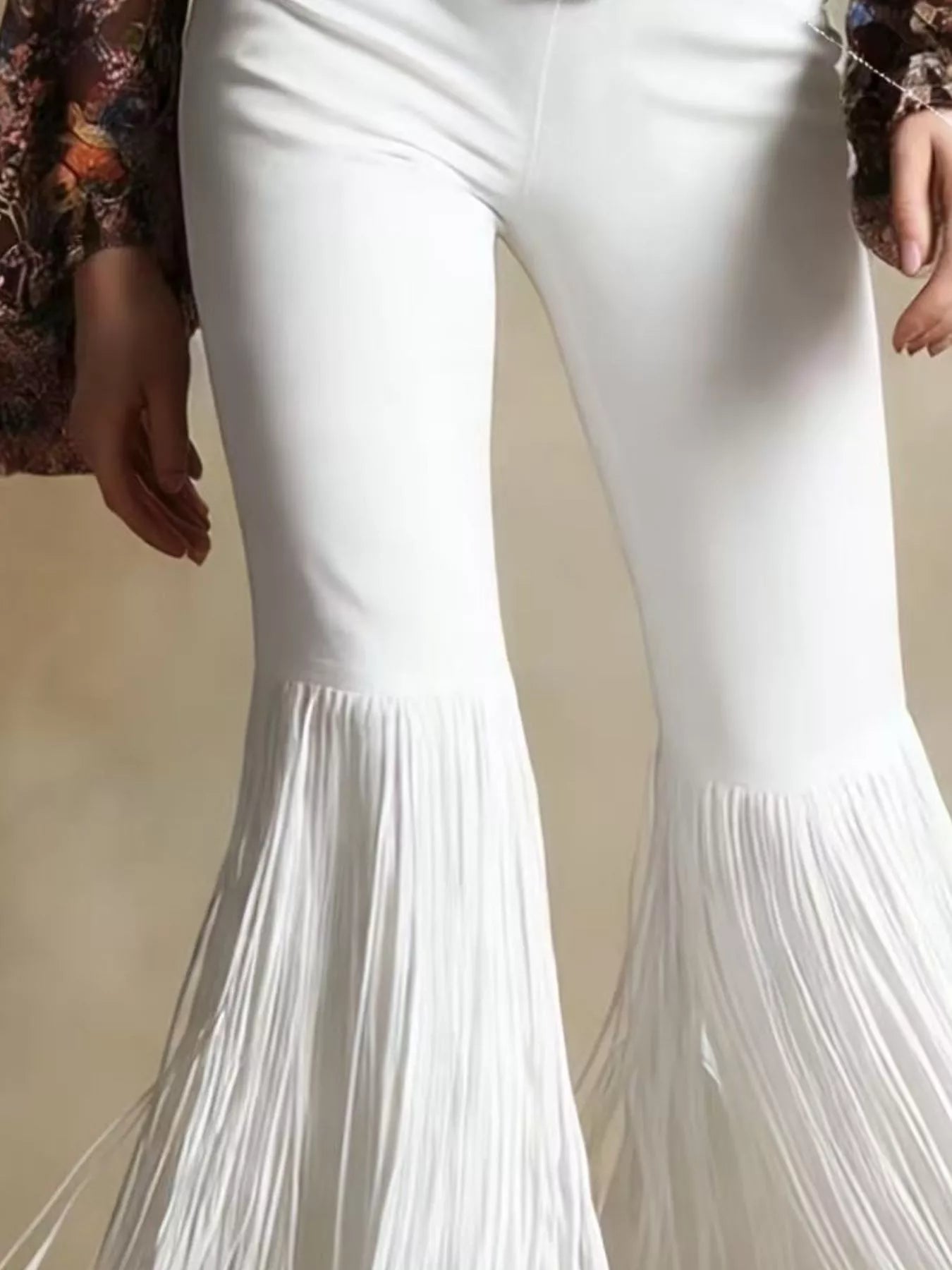 White flared pants with fringe details on a neutral background