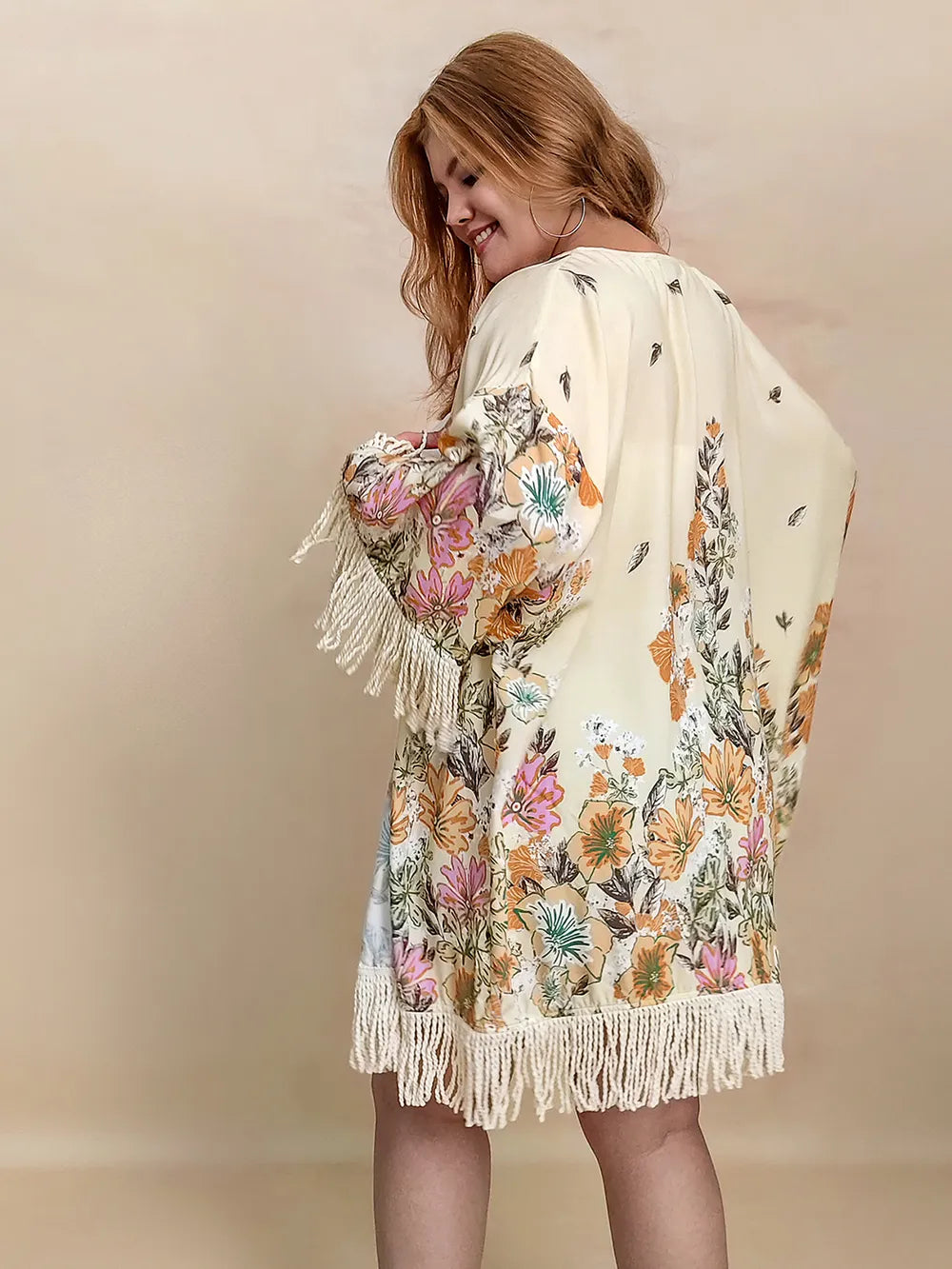 Woman wearing a floral kimono with fringes on a beige background