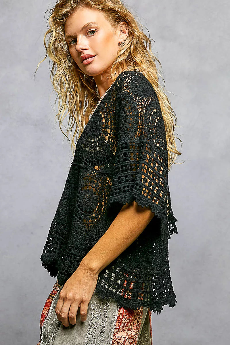 Woman wearing a black crochet top against a gray background
