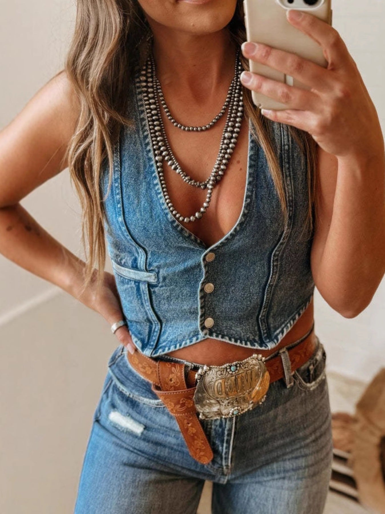 Woman wearing a denim vest and jeans, taking a selfie.