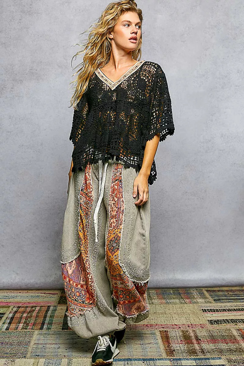 Woman wearing a black crochet top and patterned pants against a gray background