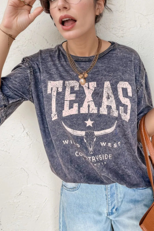 Person wearing a blue 'Texas' t-shirt with a white star and text, standing against a light-colored wall.
