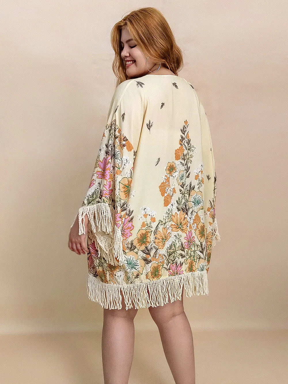 Woman wearing a floral kimono with fringes on a beige background