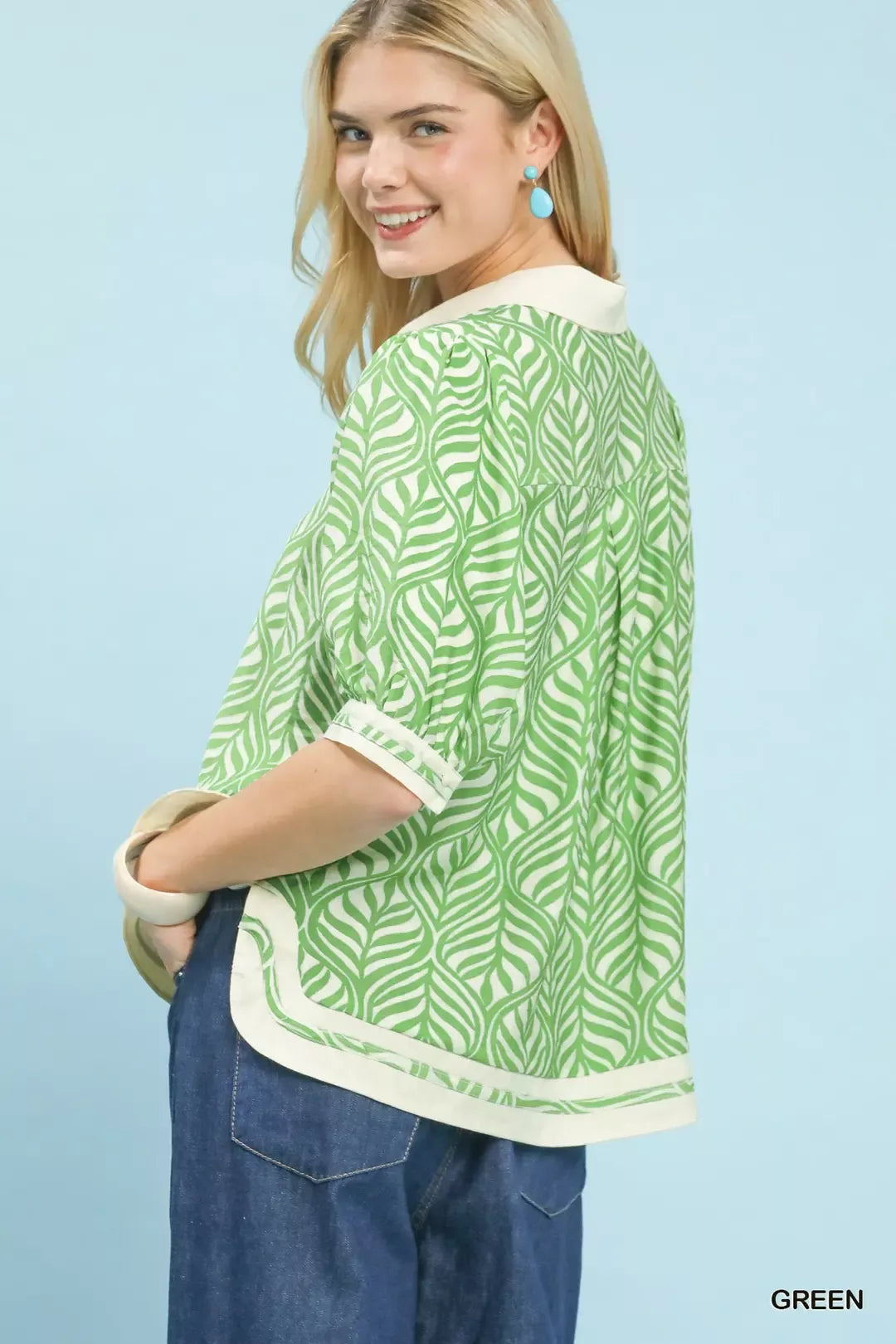 Woman wearing a green patterned top with rolled-up sleeves against a light blue background