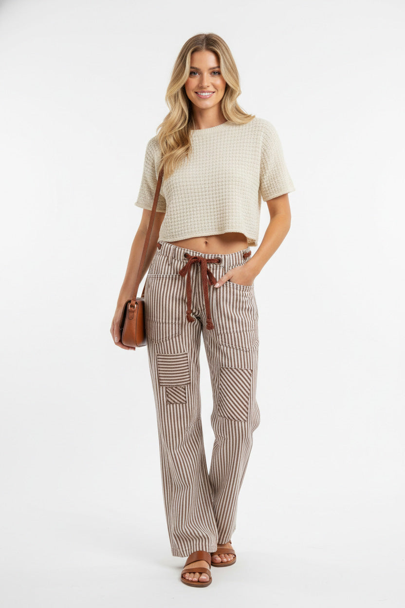 Woman wearing a beige top and striped pants on a white background