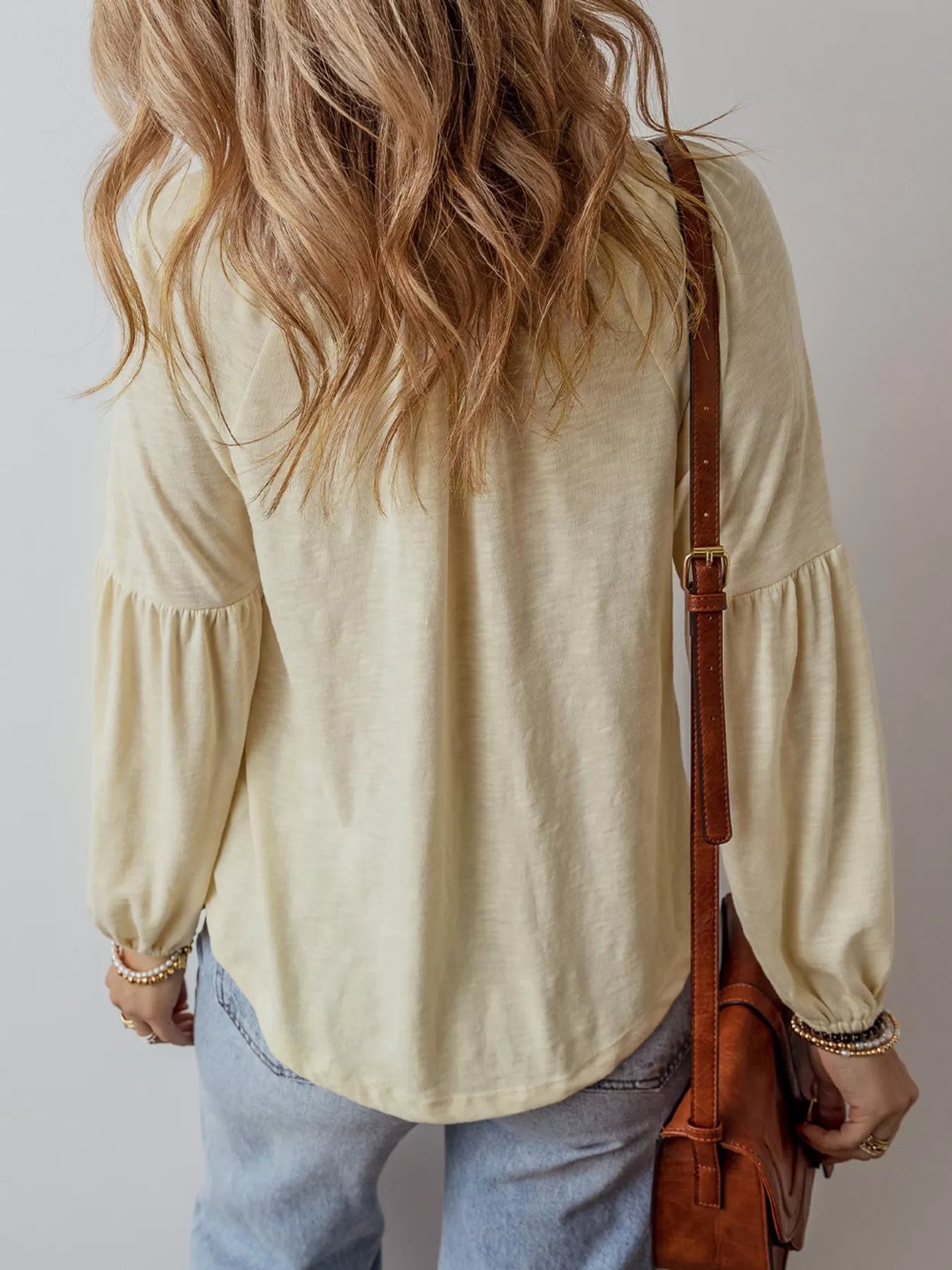 Person wearing a light-colored blouse with long sleeves and holding a brown leather bag. Back View