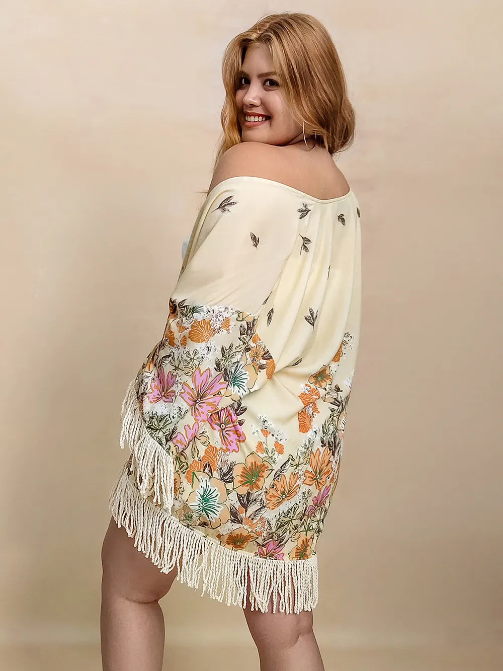 Woman wearing a floral off-shoulder top and skirt with fringe on a beige background