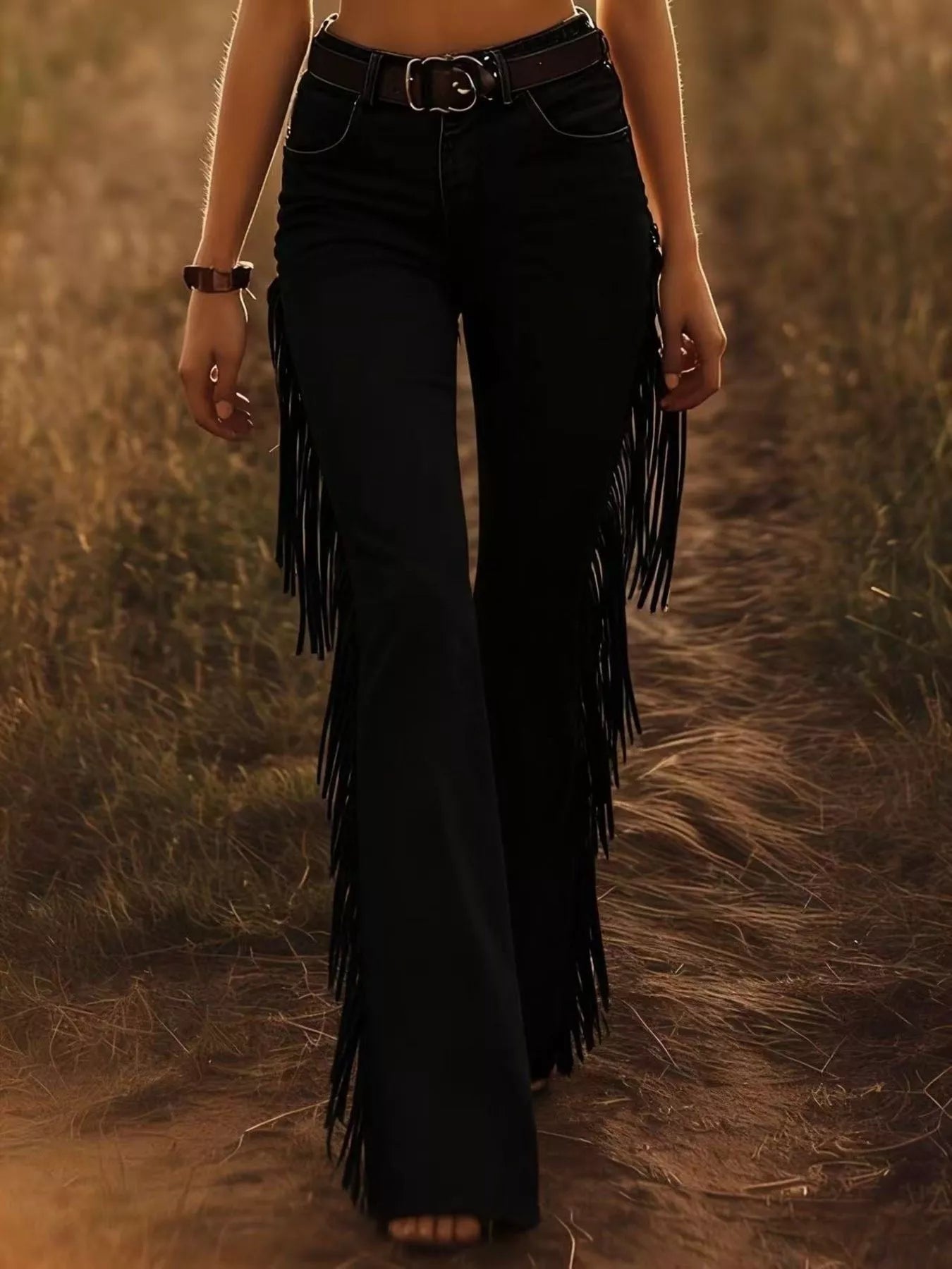 Person wearing black fringed pants standing in a field.