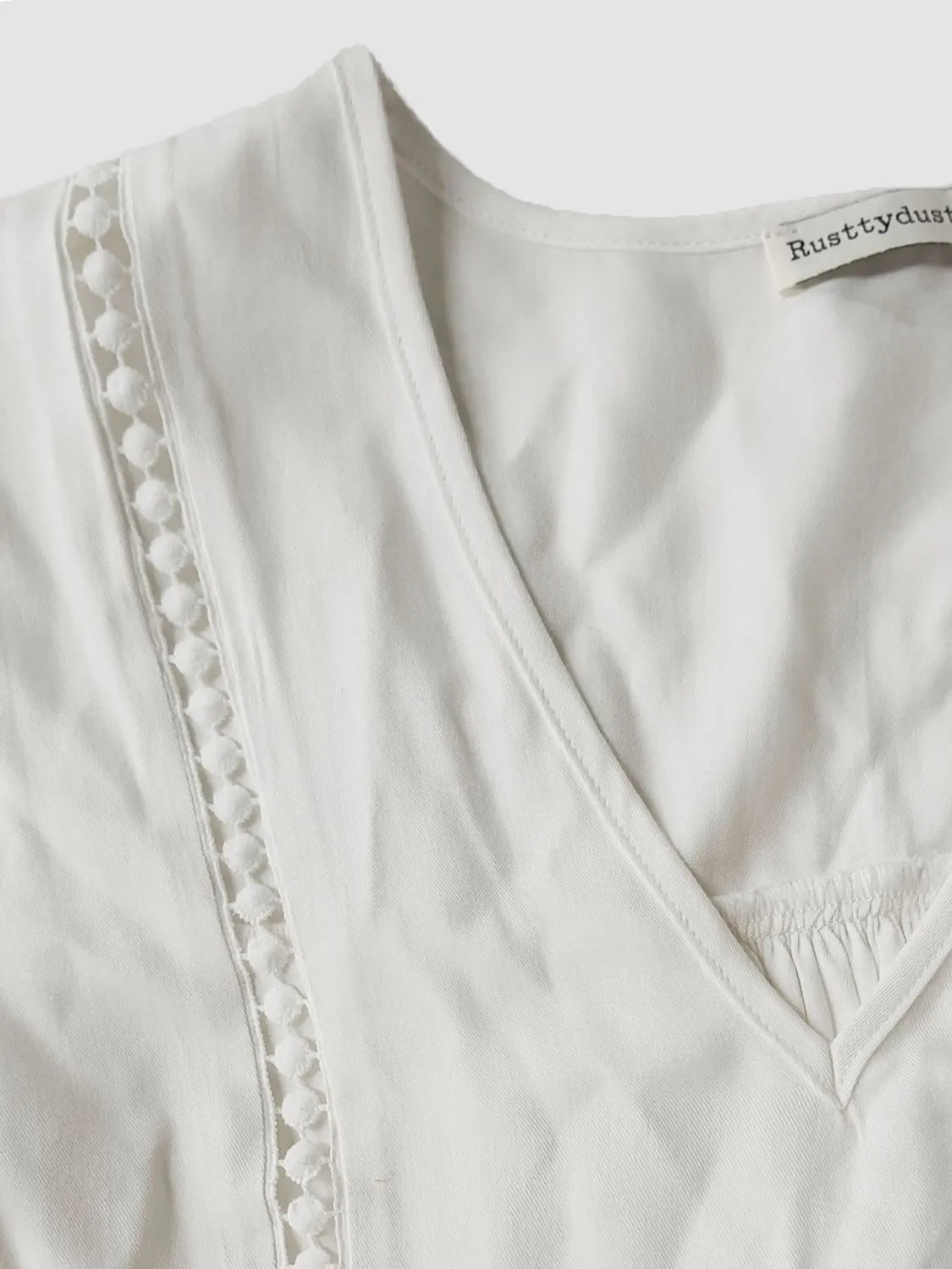 Close-up of a white garment with lace trim and 'Rustydust' branding.