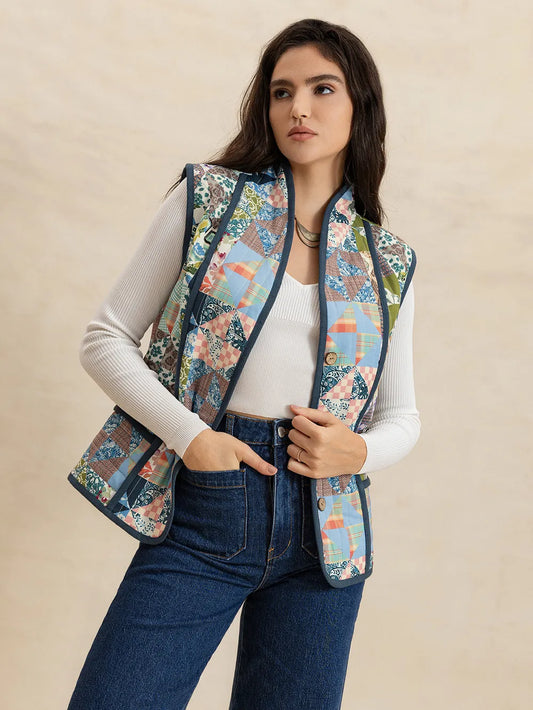 Woman wearing a floral patterned vest over a white shirt and jeans on a beige background