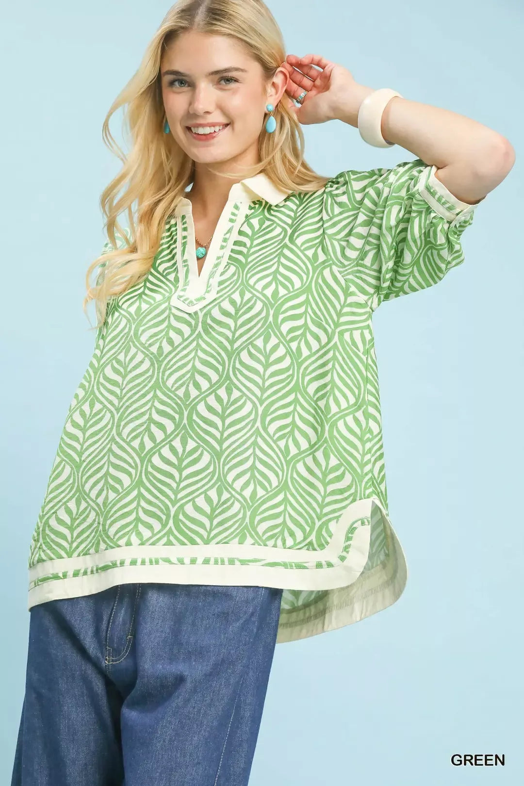Woman wearing a green patterned top with blue jeans against a light blue background