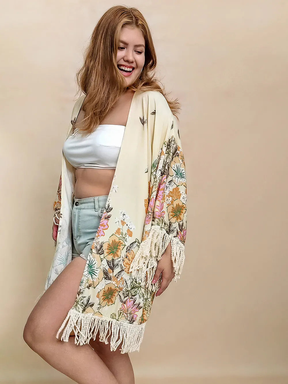 Woman wearing a floral kimono over a white top and light blue shorts on a beige background