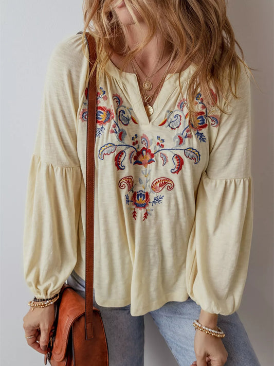 Woman wearing a cream-colored blouse with colorful embroidery, holding a brown leather bag.