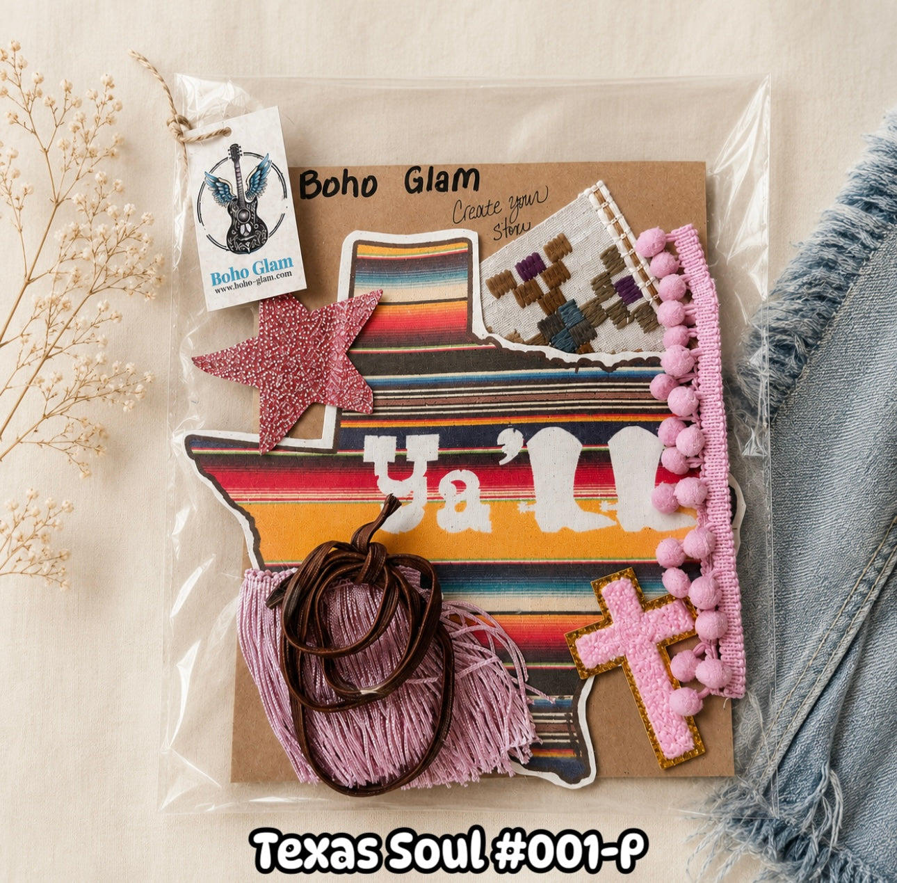 A packaged bohemian-style patch set labeled 'Boho Glam' and 'Texas Soul #001-P' on a kraft card, featuring a Texas-shaped patch with 'Ya'll', a pink glittery star, a pink cross patch, pink pom-pom trim, pink tassels, brown hair ties, and a small embroidered patch. The set is photographed on a light beige surface with dried flowers and denim fabric nearby.