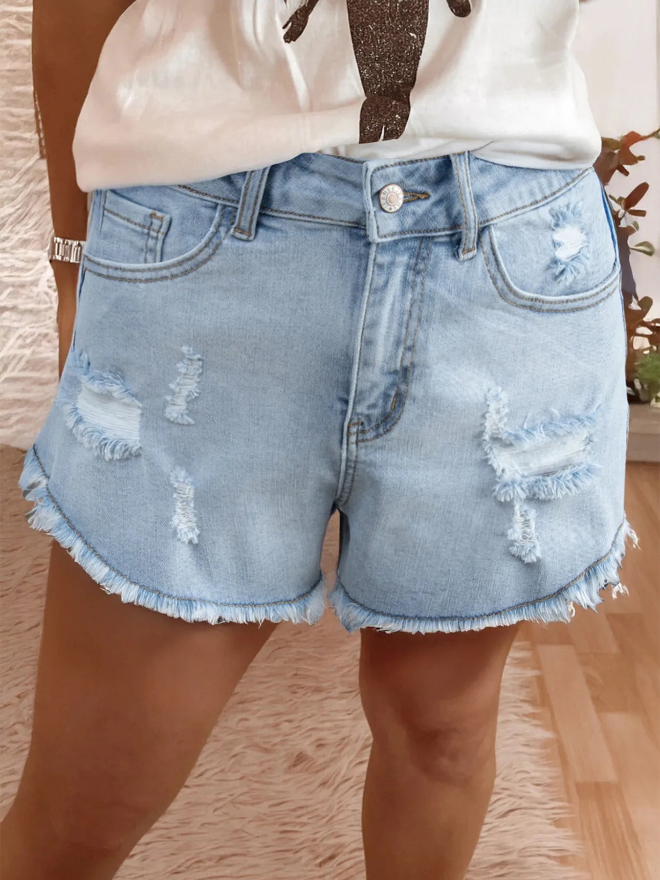 High Rise Light blue denim shorts with frayed edges worn by a person indoors.