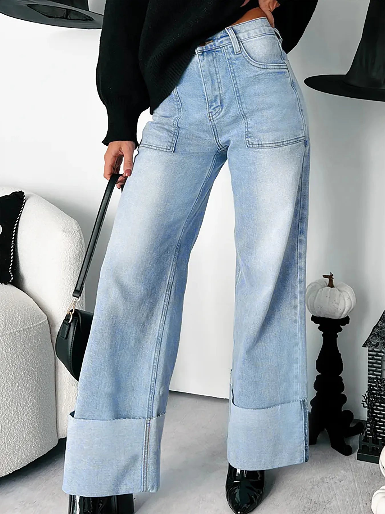 Person wearing light blue, wide leg jeans in a room with a white wall and decorative items.