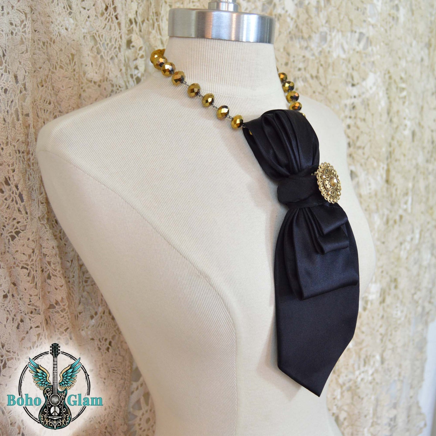 Black bow necklace with gold beads on a mannequin bust against a textured beige background.