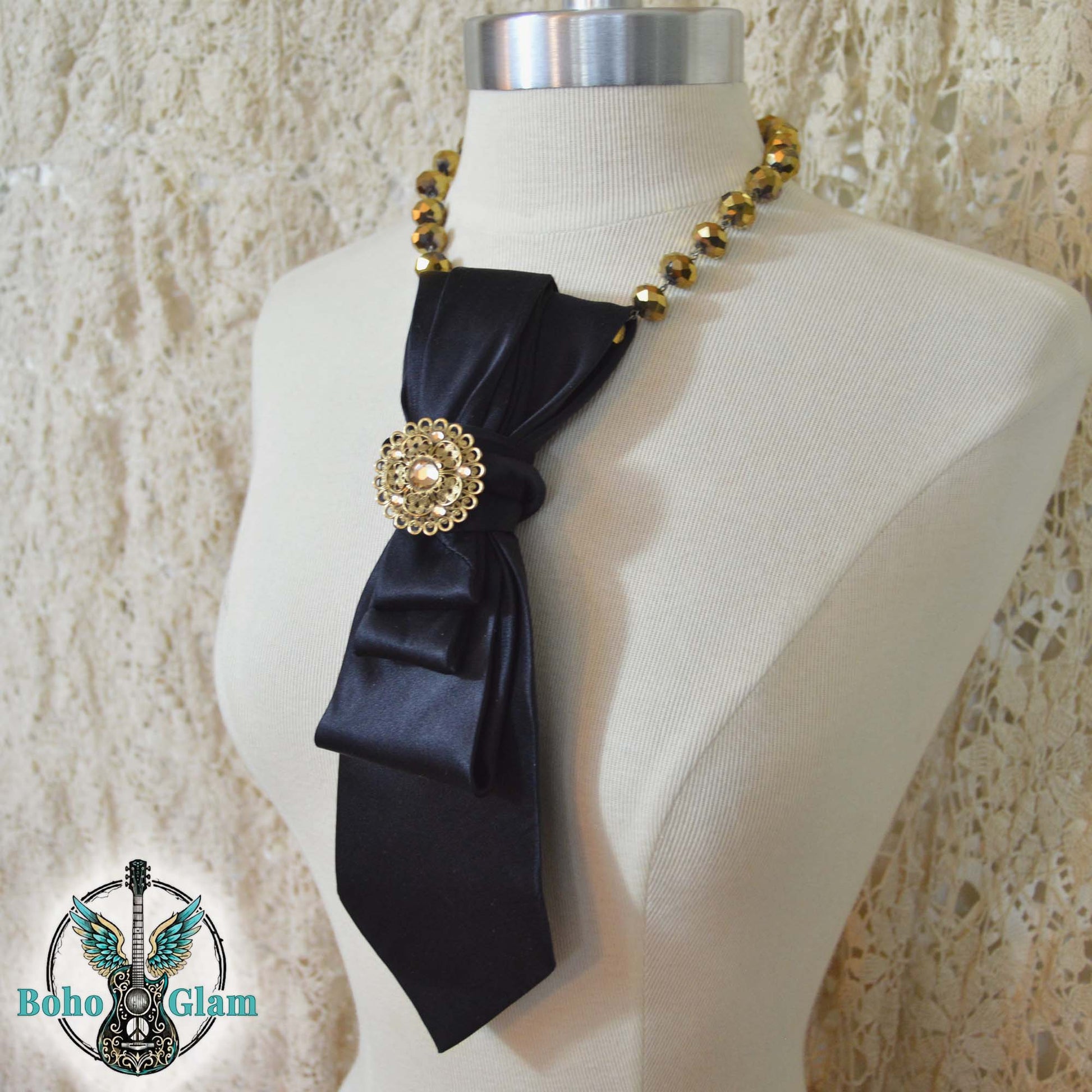 Black satin scarf with gold embellishments on a mannequin against a textured beige background, featuring the 'Boho Glam' brand.
