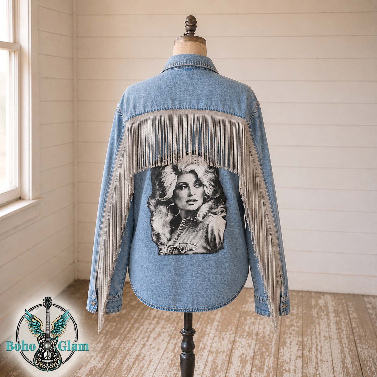 Denim jacket with fringe and graphic on a mannequin against a wooden wall.