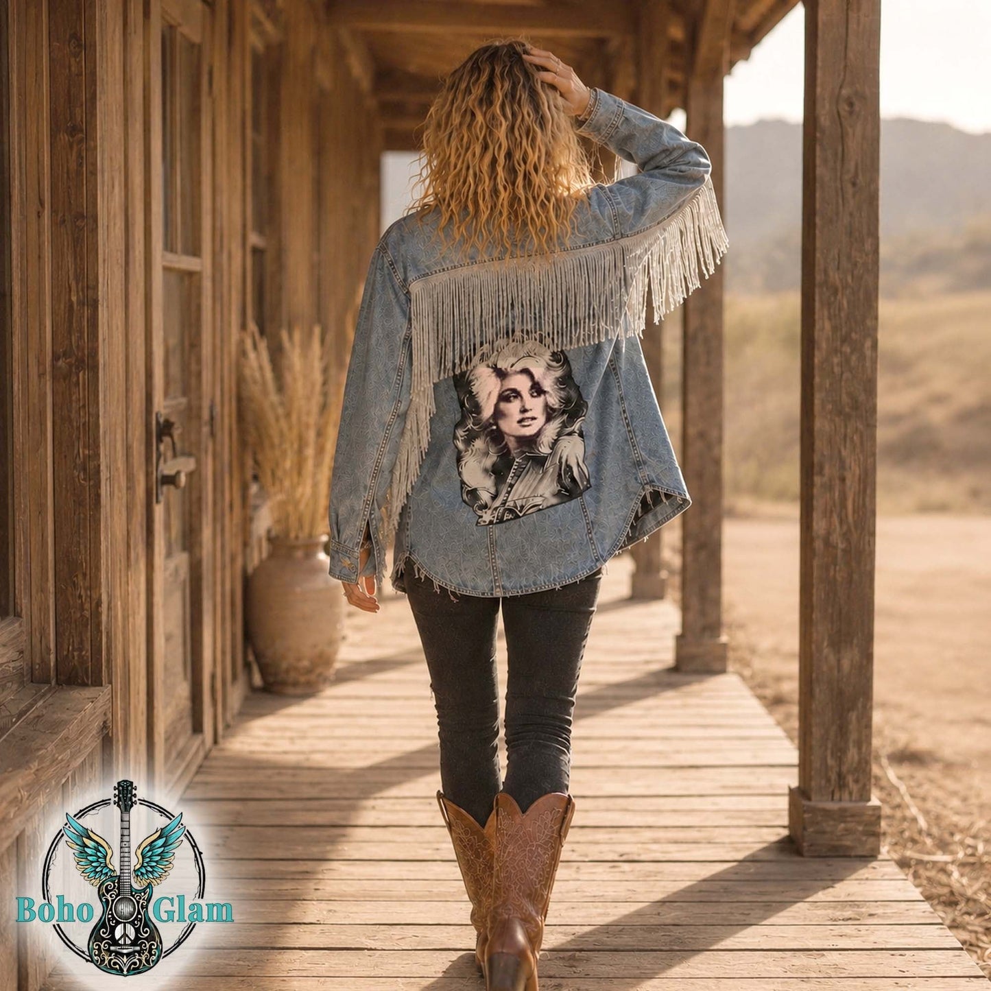 Woman wearing a denim jacket with fringe and a graphic design, standing on a wooden porch with a desert landscape in the background.