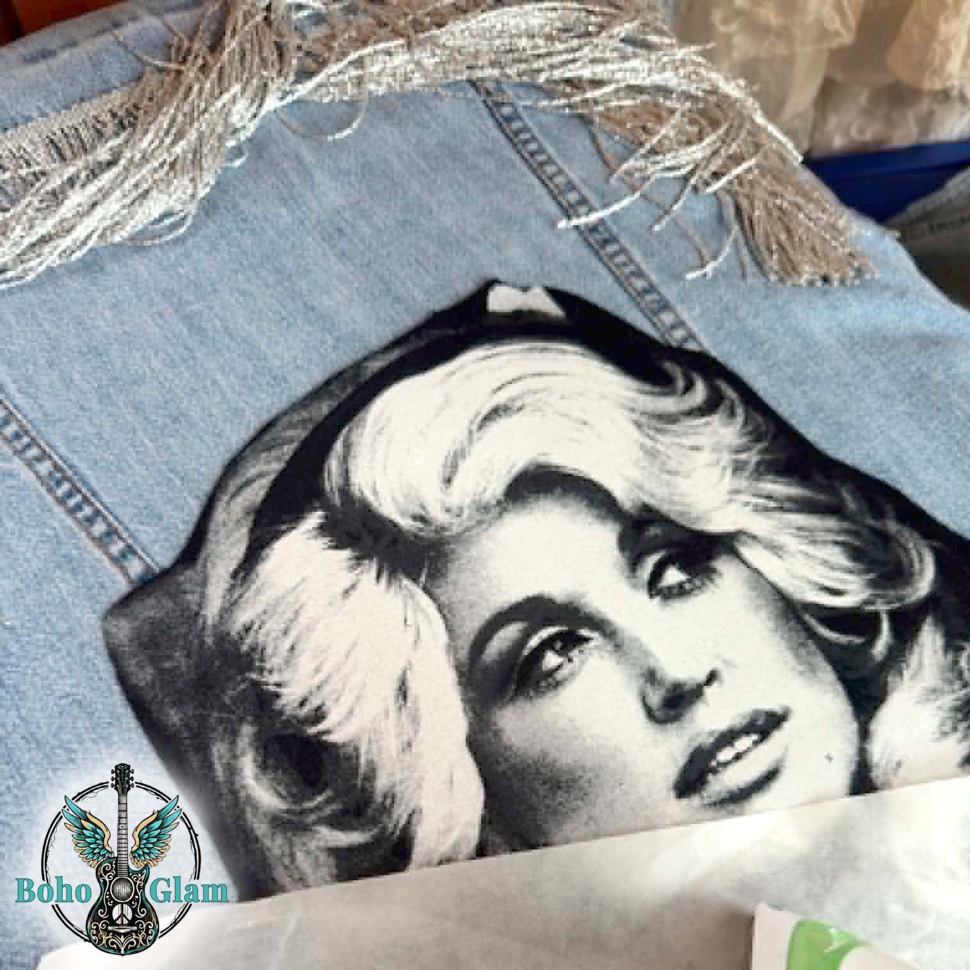 Denim jacket with a graphic of a woman's face on a textured surface, featuring the brand 'Boho Glam'.