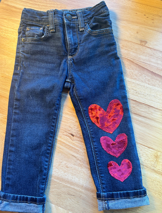 Blue jeans with pink heart designs on a wooden surface