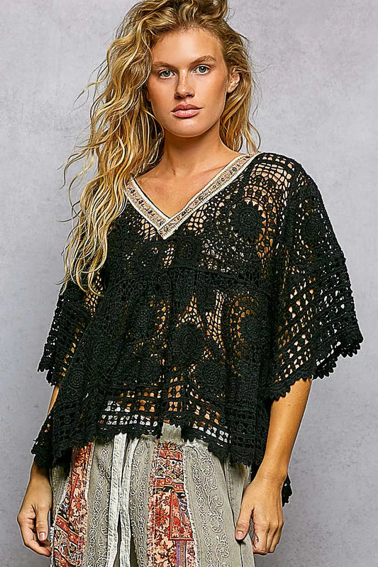 Woman wearing a black crochet top against a gray background