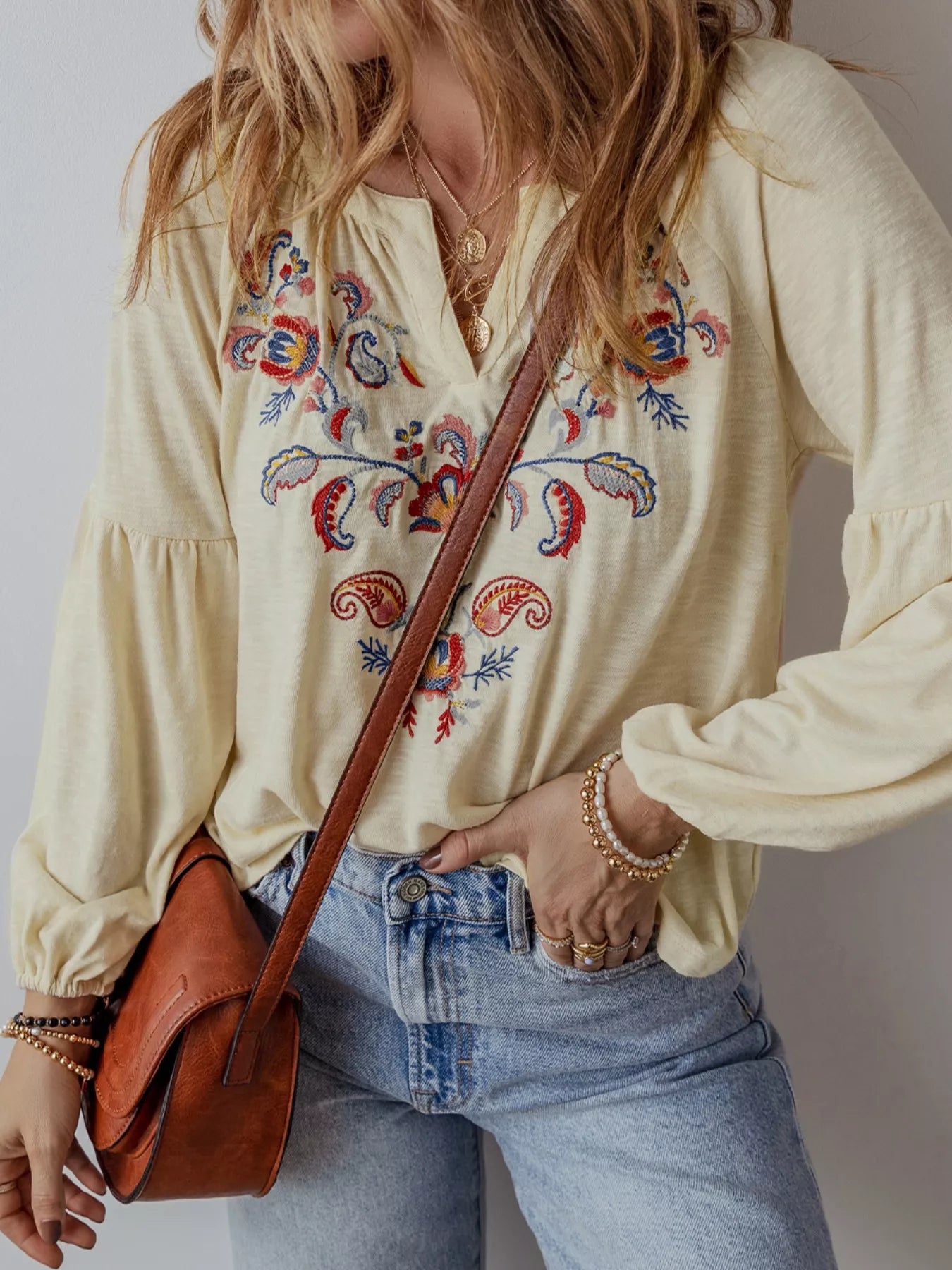 Person wearing a cream-colored blouse with colorful embroidery, holding a brown leather bag.