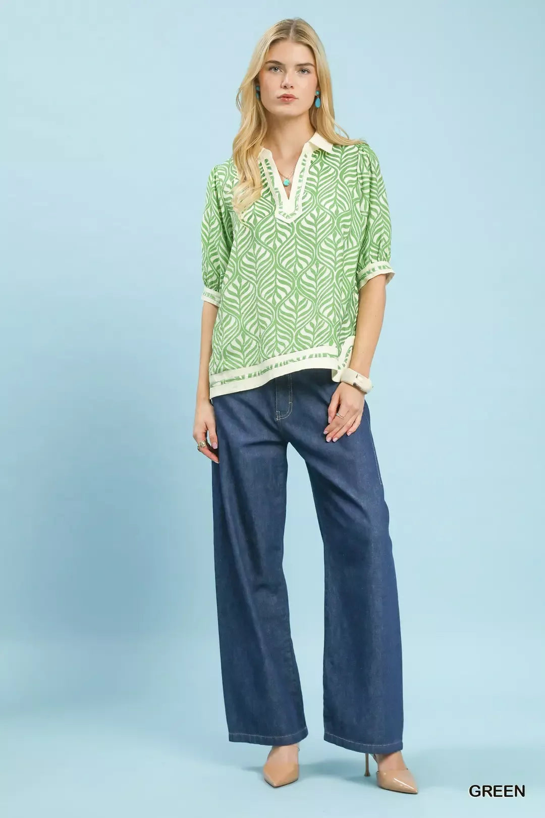 Woman wearing a green patterned top and blue jeans on a light blue background