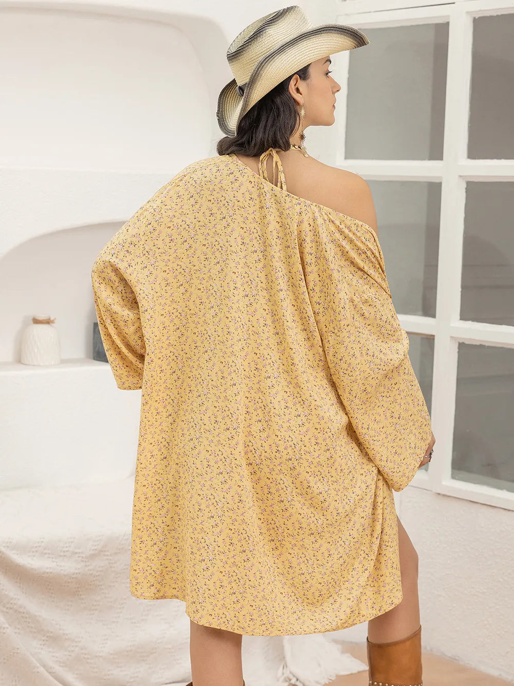 Woman wearing a yellow off-shoulder dress and straw hat in a minimalistic room.