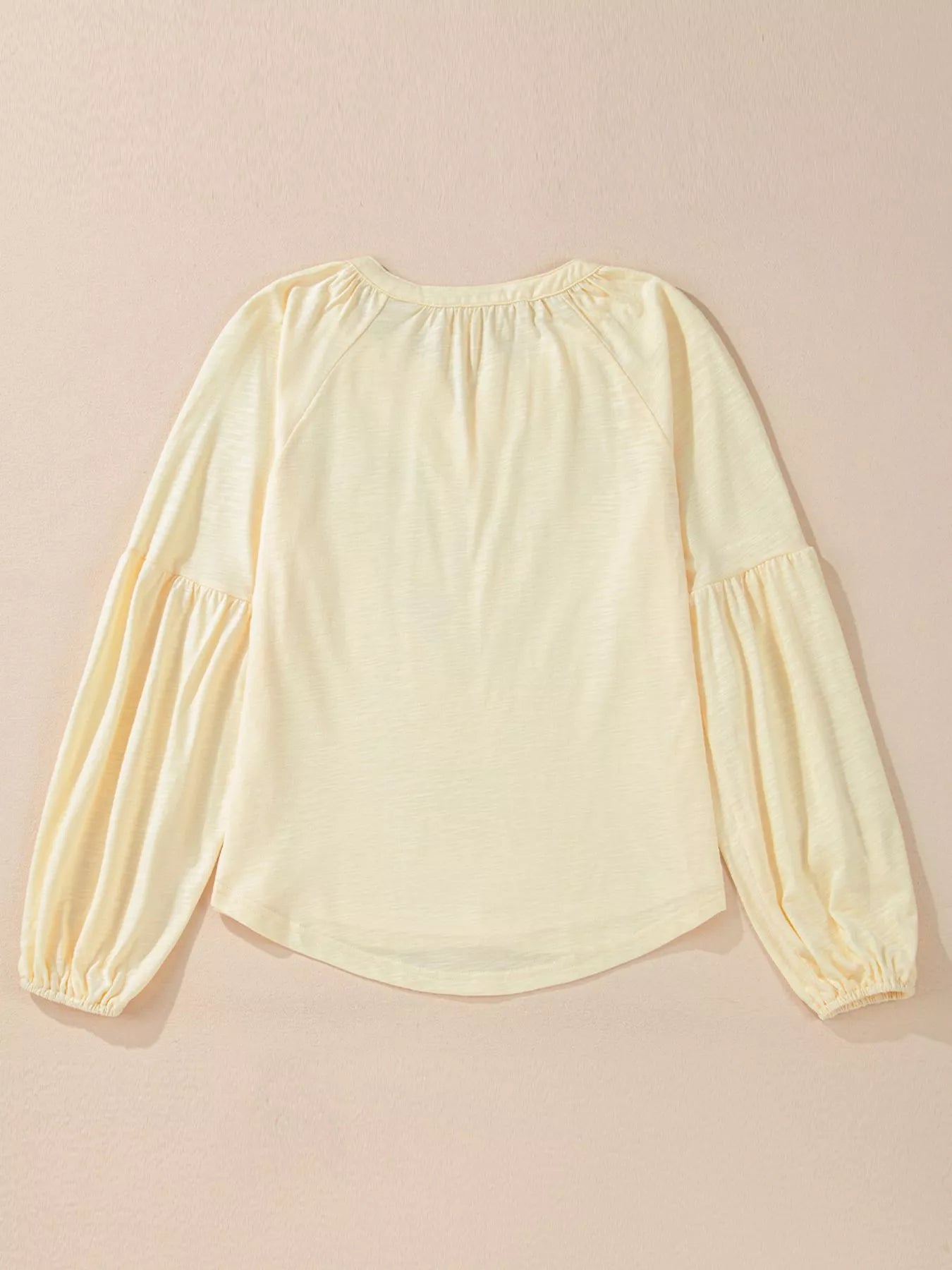 Cream colored blouse with balloon sleeves on a beige background, backside