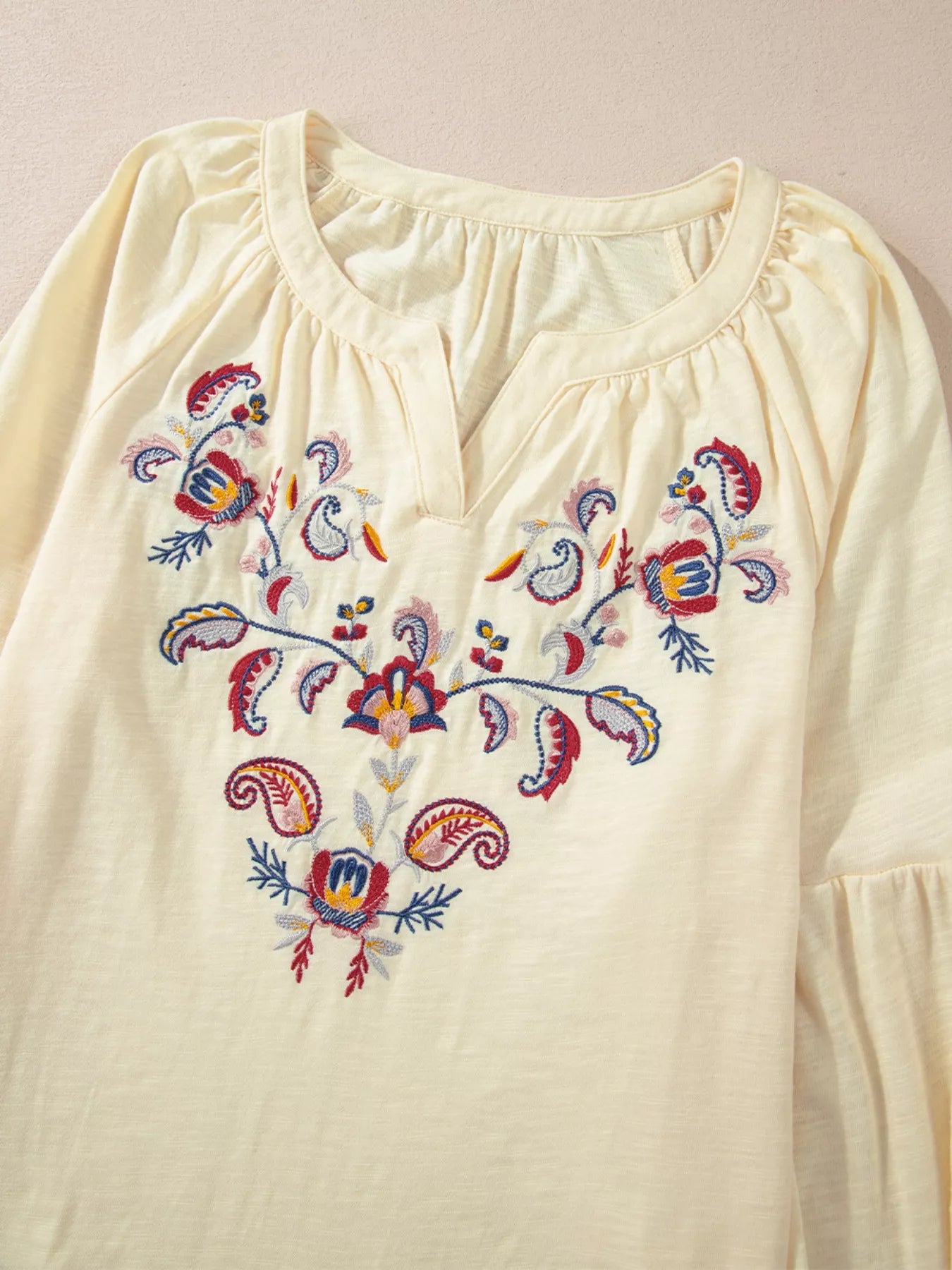 Cream-colored blouse with colorful floral embroidery on a beige background