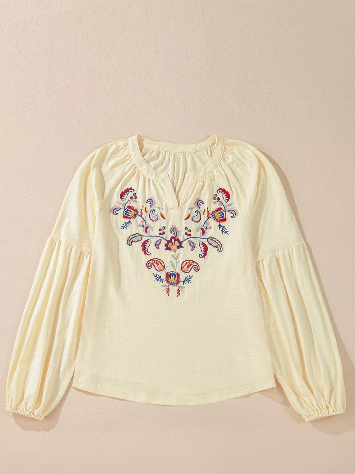 Cream colored blouse with floral embroidery on a beige background