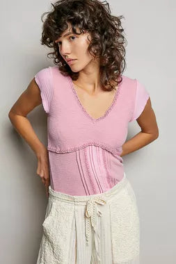 Woman wearing a pink top and white pants against a plain background