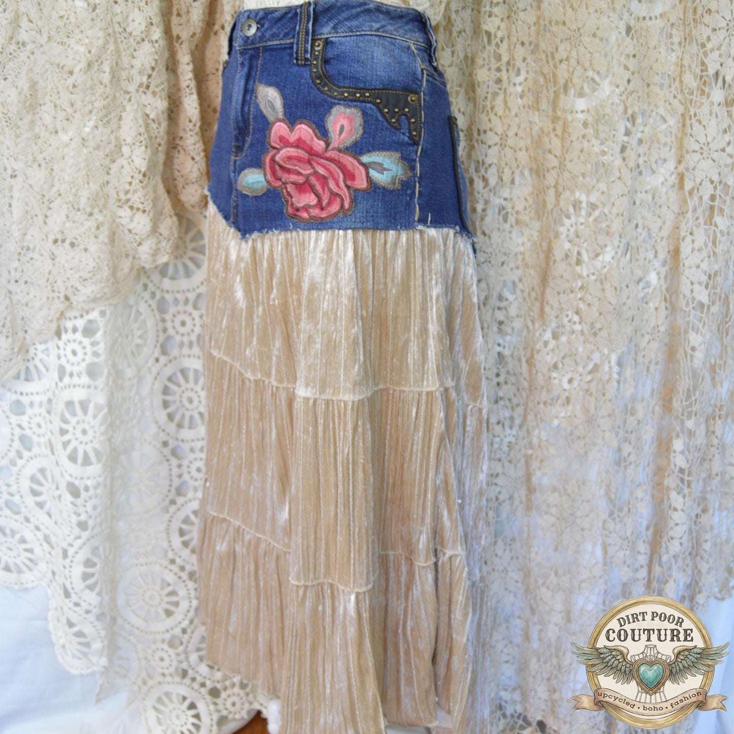 A handmade maxi skirt on a mannequin, combining a studded denim top with a flowing, champagne-colored velvet skirt featuring a red peony embroidery below the left pocket.
