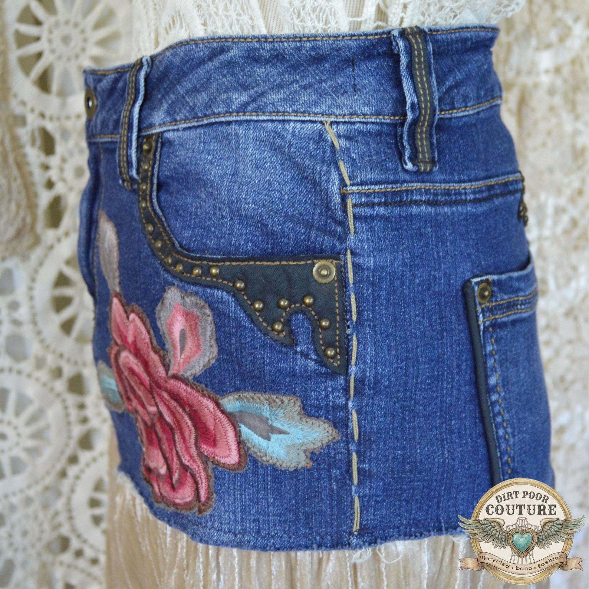 A detailed shot of the intricate red and pink peony embroidered applique below the studded denim pocket
