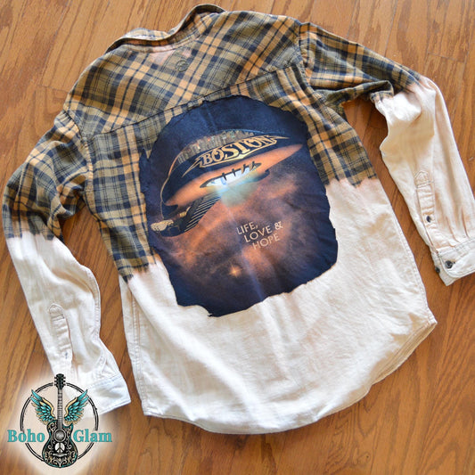 Back View: A yellow and black plaid flannel shirt with a bleached white bottom half and a large circular Boston band graphic appliqued on the back