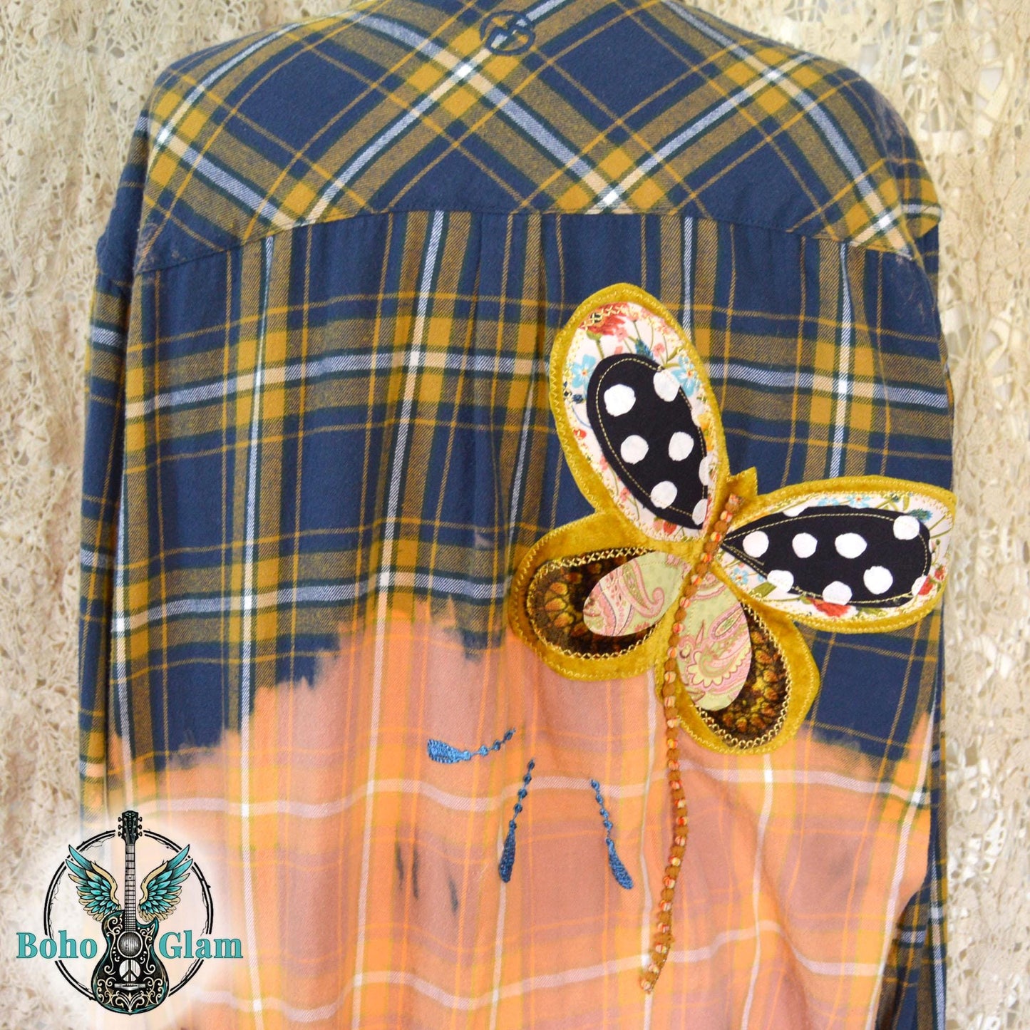 Back View: A navy and gold plaid flannel shirt with a bleached peach bottom half featuring a large butterfly applique and a 1 John 4:8 bible verse patch.