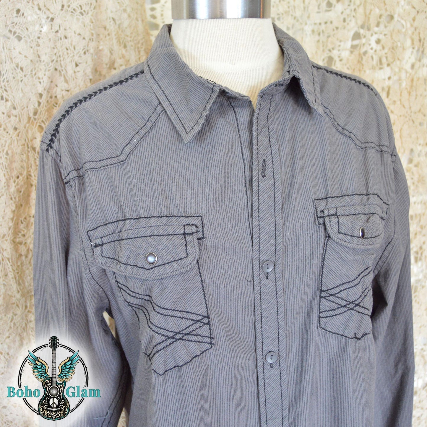 The front of a gray corduroy western shirt on a mannequin showing double chest pockets with black contrast stitching and silver snap buttons.