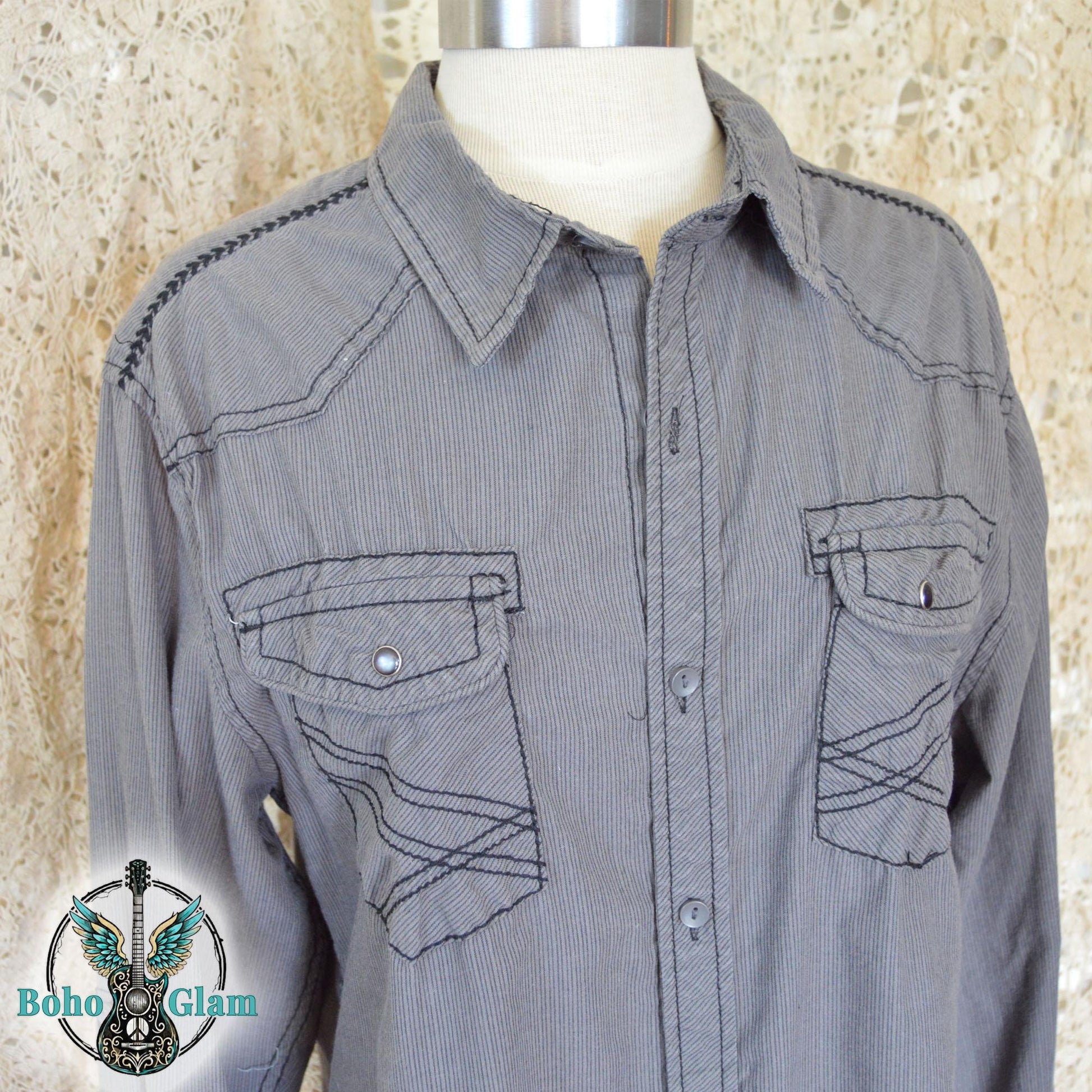 The front of a gray corduroy western shirt on a mannequin showing double chest pockets with black contrast stitching and silver snap buttons.