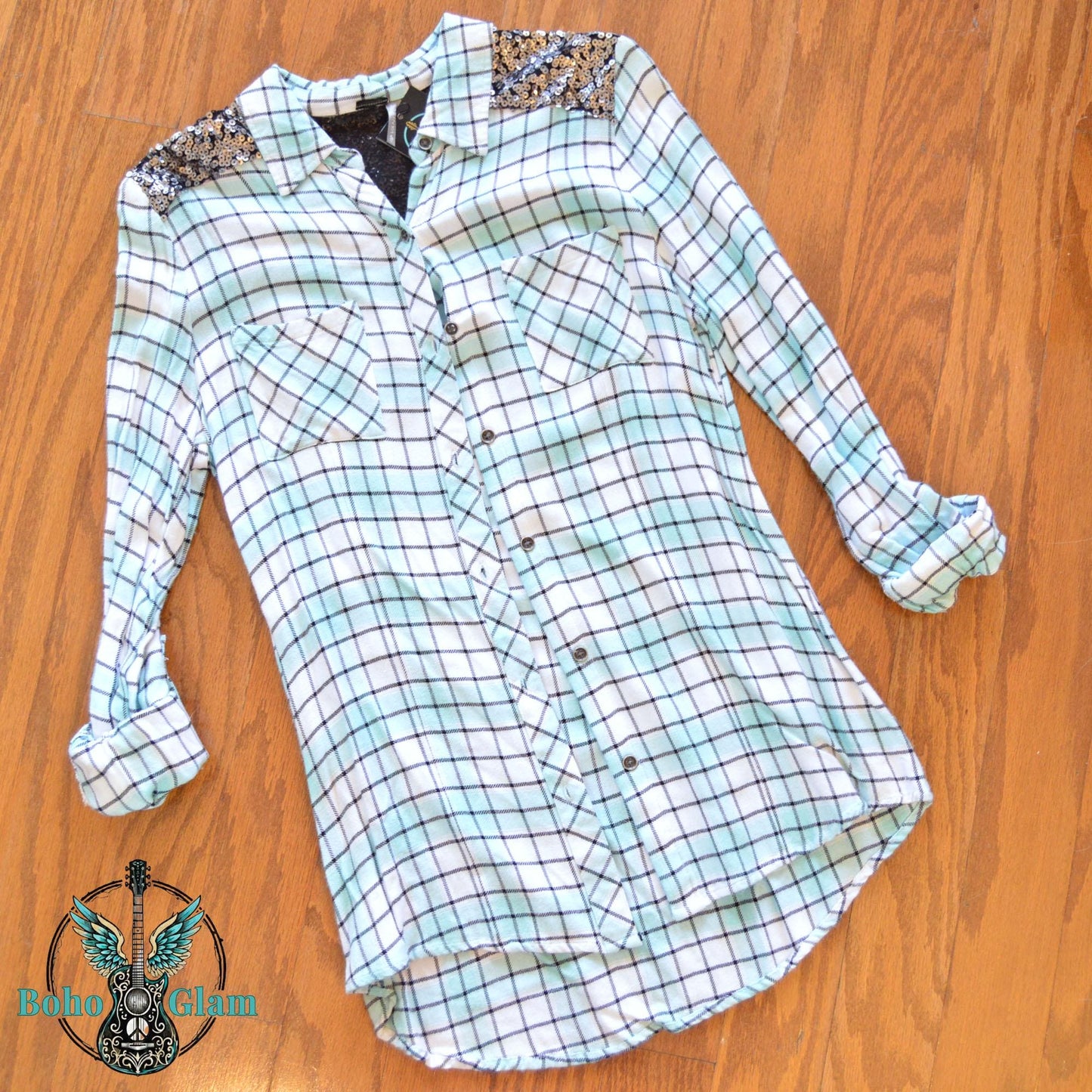 Front Flat Lay: Front view of a mint and white plaid button-down flannel with silver sequin shoulder patches laid flat on a wood floor.