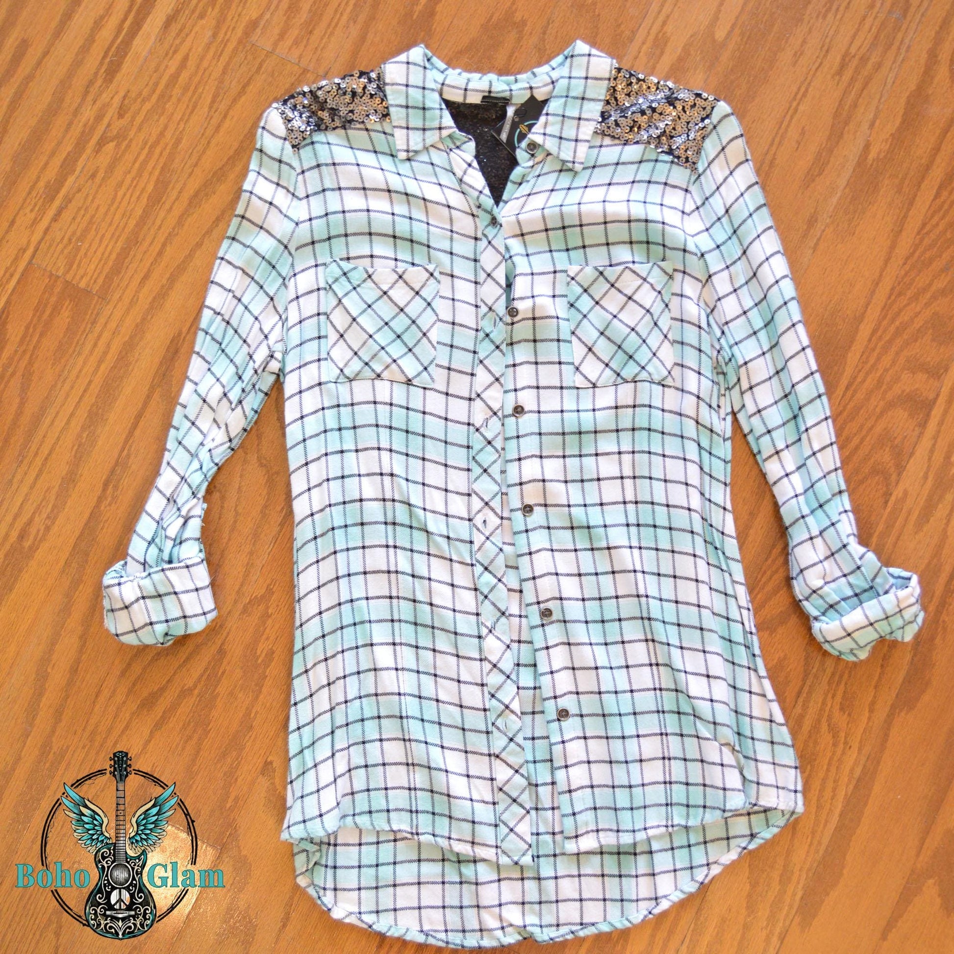 Front Flat Lay: Front view of a mint and white plaid button-down flannel with silver sequin shoulder patches laid flat on a wood floor.