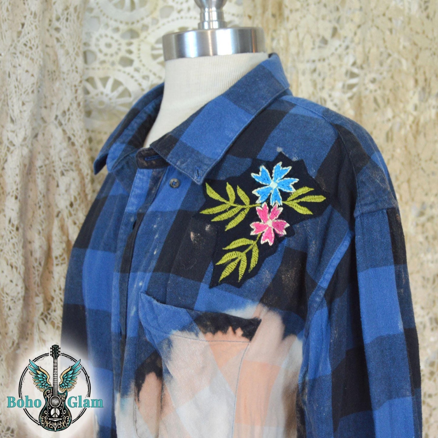 Embroidery Detail: A detailed shot of the left shoulder featuring an embroidered patch of blue and pink flowers with green leaves on the dark plaid fabric.