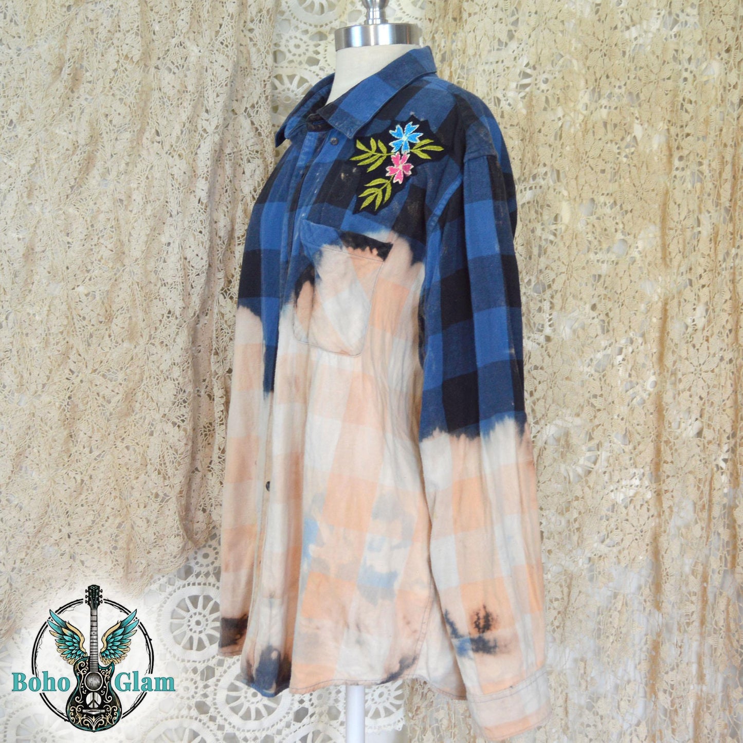 Embroidery Detail: A detailed shot of the left shoulder featuring an embroidered patch of blue and pink flowers with green leaves on the dark plaid fabric.