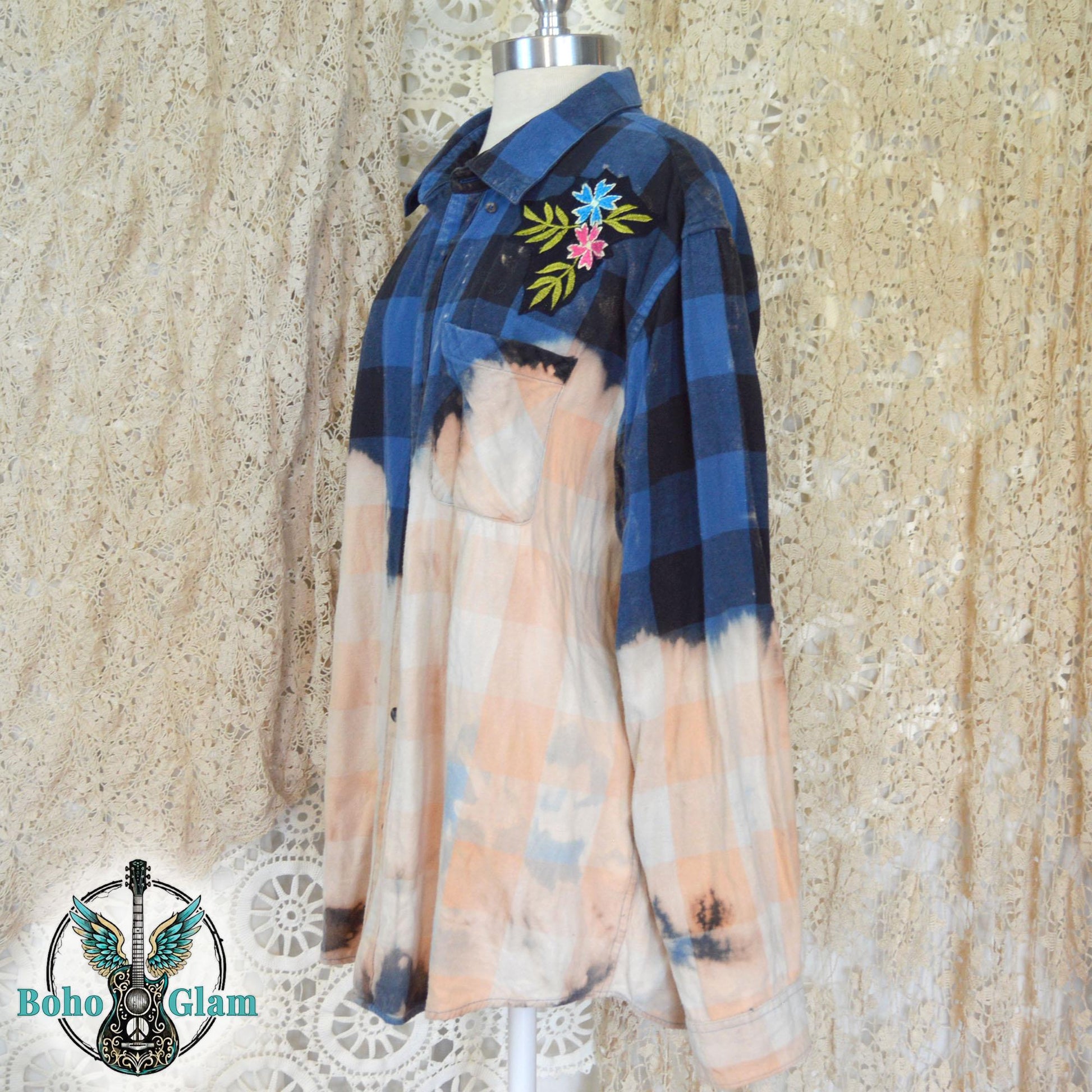 Embroidery Detail: A detailed shot of the left shoulder featuring an embroidered patch of blue and pink flowers with green leaves on the dark plaid fabric.