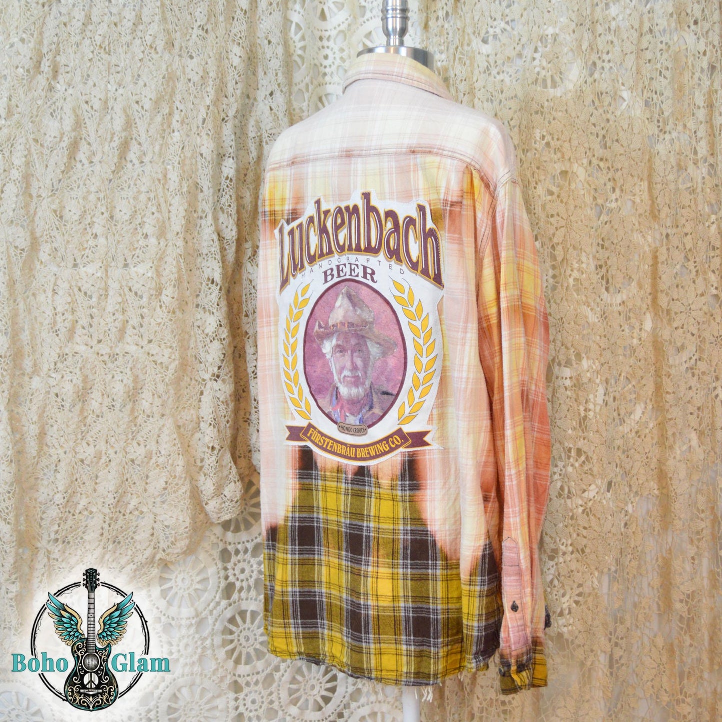 Back View: The back of a bleached plaid flannel featuring a large circular graphic for Luckenbach Beer with a portrait of Hondo Crouch.