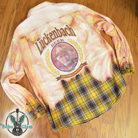 Flat Lay Back: The shirt laid flat on a wood floor to show the full scale of the Luckenbach graphic and the dip-dye bleach effect.