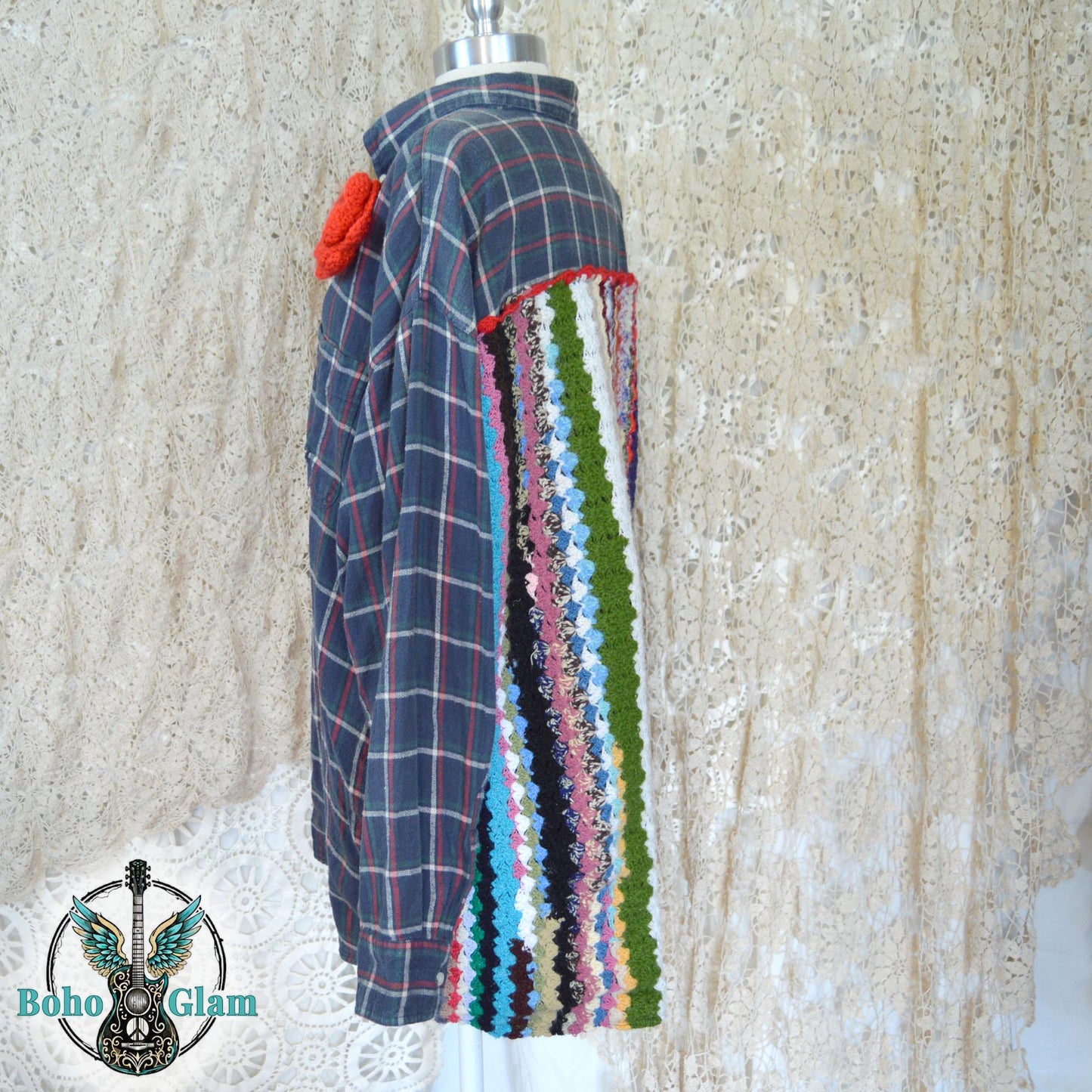Side View on Mannequin: A profile view of the shirt on a mannequin, showing the transition from the traditional plaid sleeve to the thick, textured crochet panel on the back and a large red crochet flower on the front shoulder.