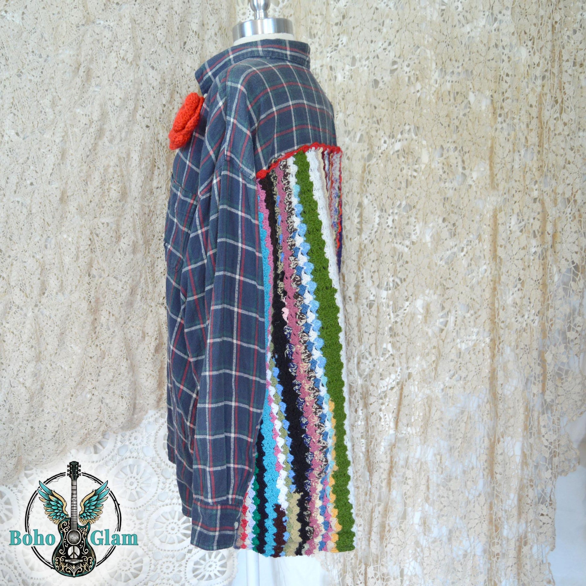 Side View on Mannequin: A profile view of the shirt on a mannequin, showing the transition from the traditional plaid sleeve to the thick, textured crochet panel on the back and a large red crochet flower on the front shoulder.